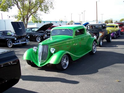 1972 Ford Ranchero - A line of custom hot rod cars are parked on asphalt, with a bright green coupe in the foreground.