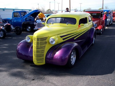 1972 Ford Ranchero - A line of custom cars, including a yellow and purple hot rod, are parked outdoors.