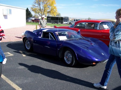 1972 Ford Ranchero - A custom-built sports car is displayed outdoors next to a vintage red car, with onlookers present.