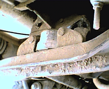1987 Ford Bronco - Close-up view of corroded vehicle undercarriage components, including suspension parts and a bolt.