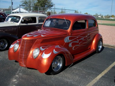 1972 Ford Ranchero - A custom orange hot rod with silver flame graphics is parked next to a brown sedan.