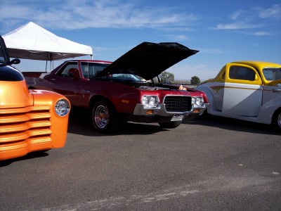 1972 Ford Ranchero - A red 1972 Ford Ranchero is displayed with its hood open, parked alongside other vehicles under a sunny sky.