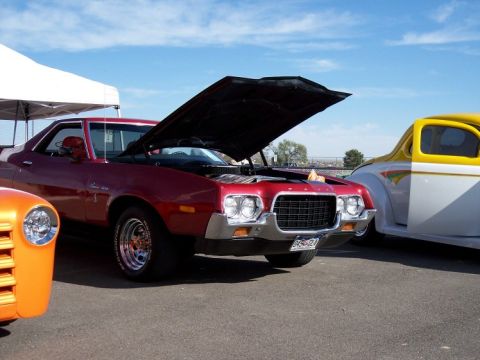 1972 Ford Ranchero - A red 1972 Ford Ranchero is displayed with its hood open, parked alongside other vehicles under a bright sky.