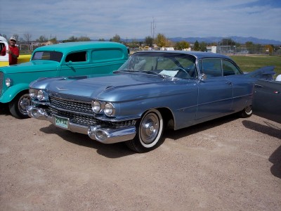 1972 Ford Ranchero - A classic blue Cadillac coupe is parked outdoors next to a teal panel van under a partly cloudy sky.