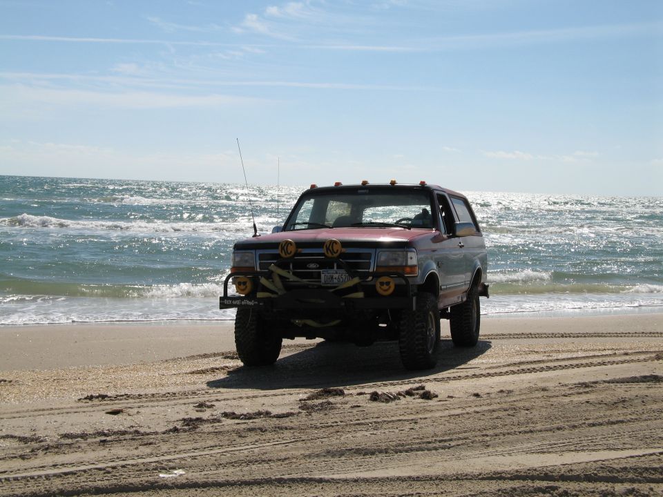 Lifted red Ford Bronco with KC lights on a beach by the ocean