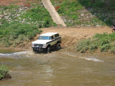 1992 Ford Mustang - A lifted Ford Bronco navigates a shallow river crossing on a dirt path.