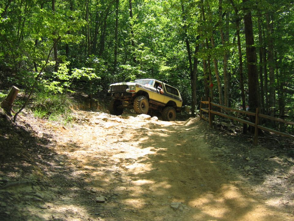Yellow off-road SUV driving up a rocky dirt path in a wooded area