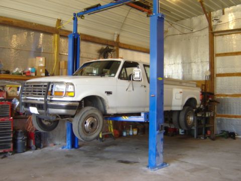 1992 Ford Bronco - A white Ford F-350 dually pickup truck is elevated on a blue hydraulic lift inside a garage.
