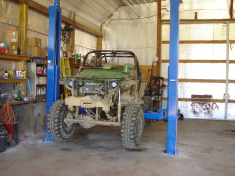 1992 Ford Bronco - A green Suzuki Samurai sits on a lift in a workshop, ready for repairs or modifications.