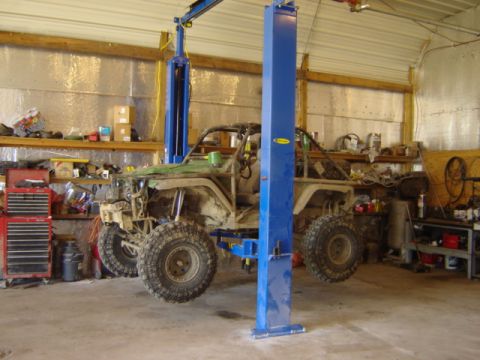 1992 Ford Bronco - Modified off-road vehicle with large tires is raised on a car lift inside a garage.