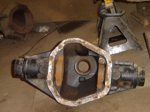1992 Ford Bronco - A differential housing sits on the floor next to a jack stand, with a partial view of another component in the background.