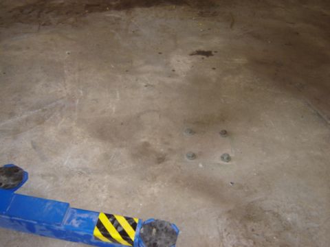 1992 Ford Bronco - A blue lift arm with hazard stripes rests on a concrete floor, with visible bolts in the ground.