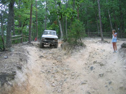 1992 Ford Mustang - Off-road vehicle navigates a challenging dirt path surrounded by trees.