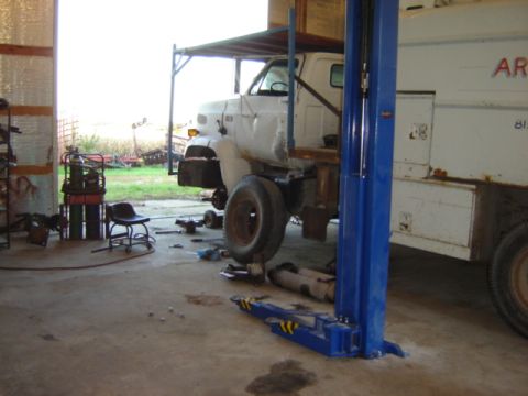 1992 Ford Bronco - A white truck is undergoing maintenance in a garage, with its front wheel removed and placed on the ground.