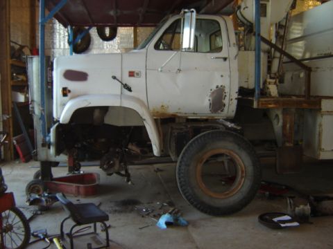 1992 Ford Bronco - White truck cab with a flatbed in a workshop, undergoing mechanical work with parts removed.