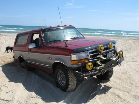 1995 Ford Bronco - Maroon-over-silver mid-1990s Ford Bronco XLT parked on a beach with ocean surf behind, black tubular prerunner-style front bumper with a bu…