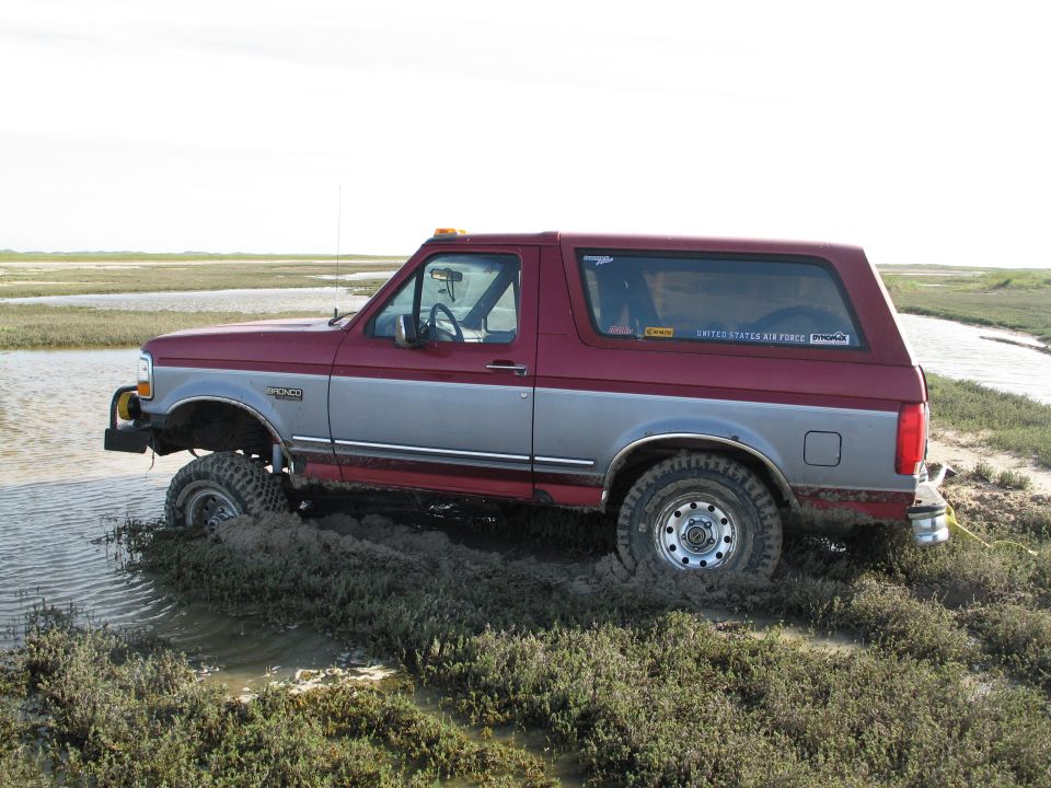 Two-tone maroon and silver Ford Bronco stuck in marsh mud, side view