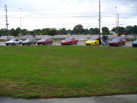 1991 Ford Probe - A line of sports cars, including a red 1991 Ford Probe, are parked on asphalt next to a grassy area.