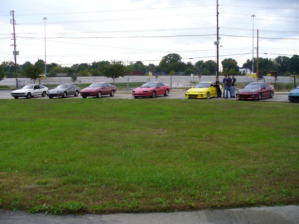 Several sports cars parked in a line, including a red 1991 Ford Probe, a yellow car, and a dark red coupe