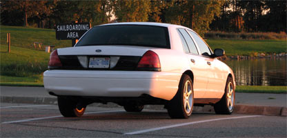 2003 Ford Crown Victoria - Small banner-crop photo of a white Ford Crown Victoria sedan viewed from three-quarter rear in a parking lot at sunset, with a blacked-out…