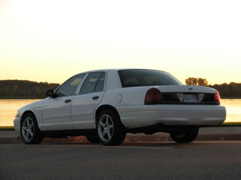 2003 Ford Crown Victoria - White Ford Crown Victoria sedan shot from the rear three-quarter angle beside a lake at golden hour, with tinted windows and a blacked-out…