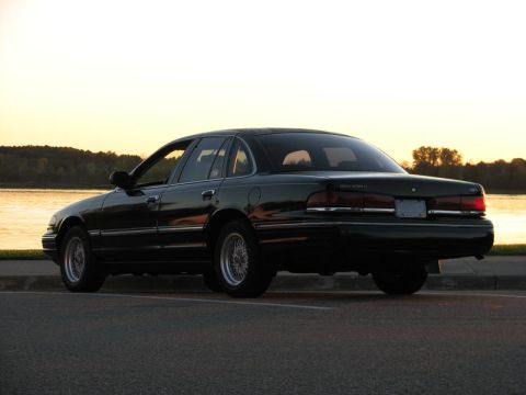 2003 Ford Crown Victoria - A dark-colored Ford Crown Victoria is seen from the rear quarter angle near a body of water as the sun sets.