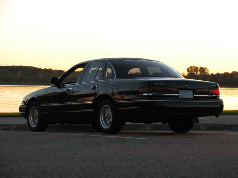 Black Ford Crown Victoria parked by a lake at sunset