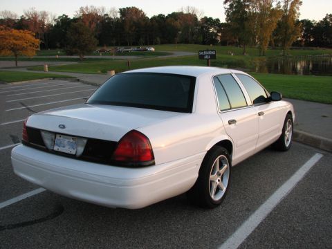 2003 Ford Crown Victoria - A white Ford Crown Victoria sedan viewed from the rear three-quarter angle in a lakeside parking lot at golden hour, with heavily tinted wi…