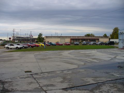 1991 Ford Probe - A group of cars are parked on a grassy area outside a commercial building.