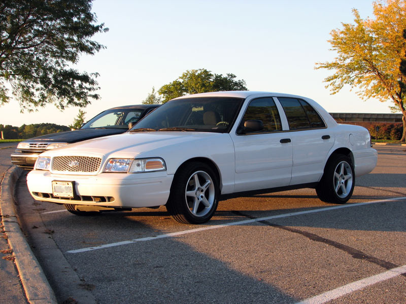 White Ford Crown Victoria sedan, 3/4 front view, with silver wheels in a parking lot