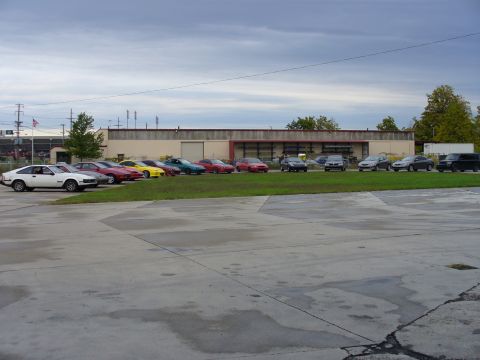 1991 Ford Probe - A row of cars, including a white 1991 Ford Probe, are parked outside a building under a cloudy sky.