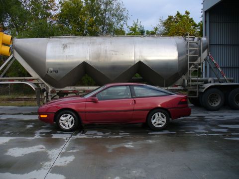 1991 Ford Probe - A maroon/burgundy 1990s Ford Probe two-door hatchback coupe shown in profile (driver's side), parked on wet concrete with silver alloy whee…