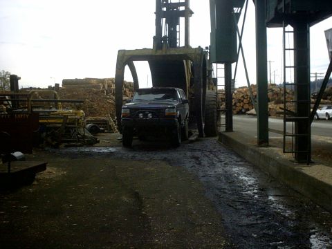 1995 Ford Bronco - A dark SUV, possibly a 1995 Ford Bronco, is being lifted by a large log loader in an industrial setting.