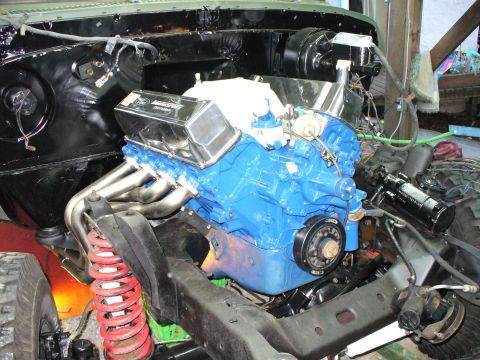 1978 Ford Bronco - A Ford blue V8 sits freshly installed in a stripped engine bay, wearing chrome Ford Motorsport valve covers, stainless shorty headers, a fl…