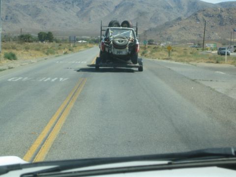 1990 Ford Bronco - off-road race vehicle numbered 301 rides on a trailer down a desert highway, framed by the towing vehicle's dash and wiper.