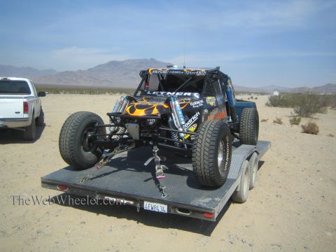 1990 Ford Bronco - Front three-quarter view of a black Letner Racing off-road buggy with flame paint chained down on a flatbed trailer in the desert.