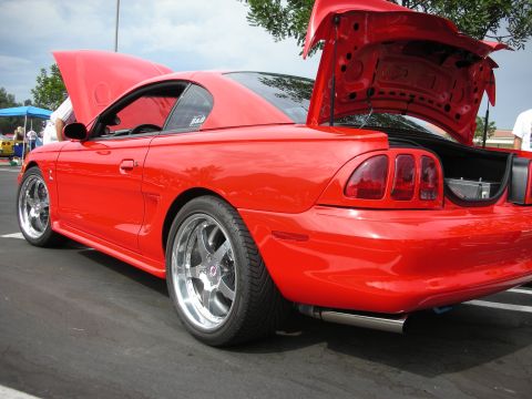 1992 Ford Crown Victoria - A bright red coupe, possibly a Ford Mustang, is displayed with its hood and trunk open, revealing custom wheels and exhaust pipes.