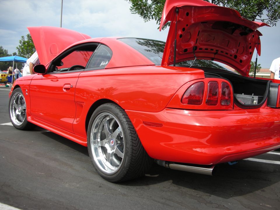 Red coupe with hood and trunk open, showing custom wheels and exhaust