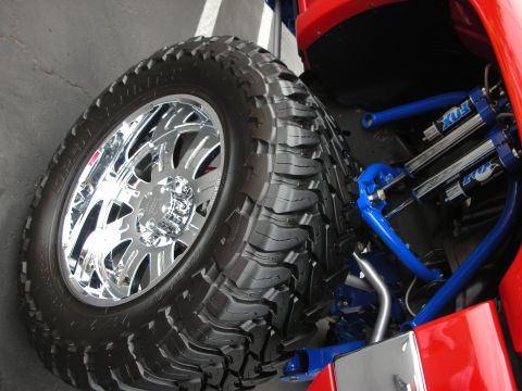 1992 Ford Crown Victoria - This image shows the custom suspension and wheel assembly of a vehicle, bright blue Fox shocks and a large, aggressive tire.