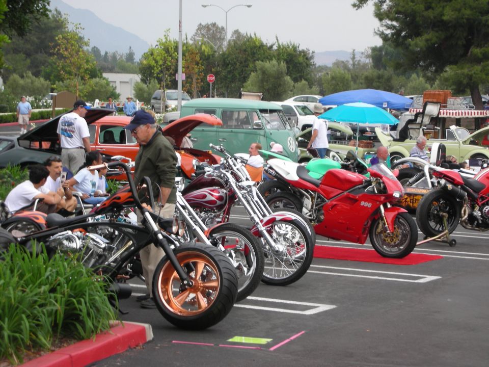 Row of custom motorcycles and classic cars at an outdoor event