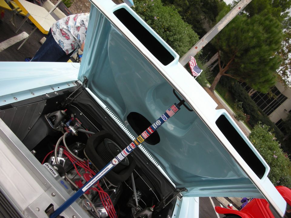 Light blue car hood open, showing engine and a blue rod with stickers