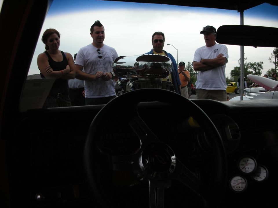 Interior view of a car with a chrome engine blower and people looking
