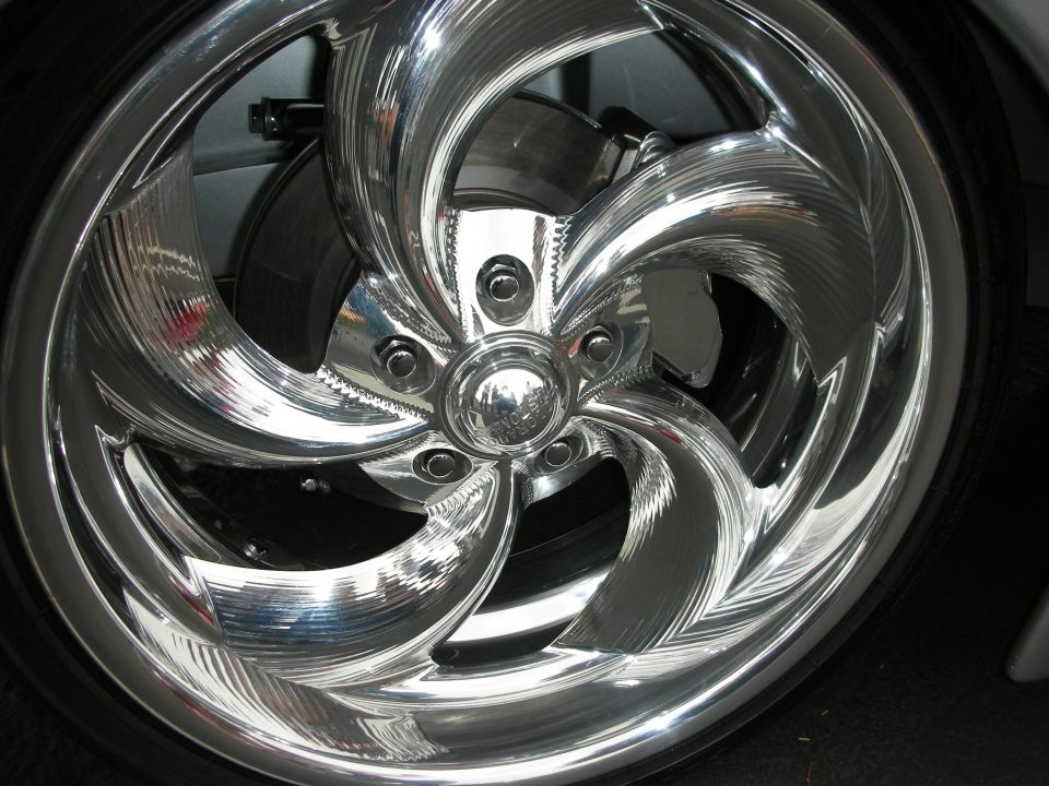 Close-up of a shiny, custom chrome wheel with a swirling spoke design