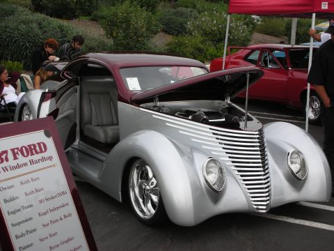 1992 Ford Crown Victoria - A customized 1937 Ford coupe with its hood open, displayed at a car show. A red car is visible in the background.