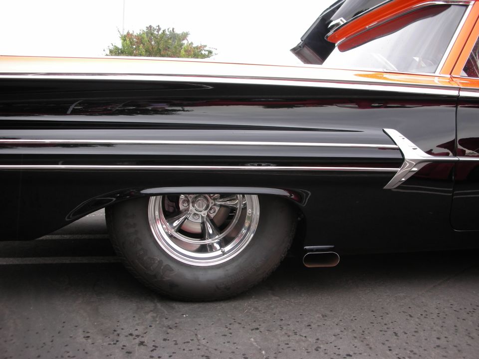 Close-up of a black hot rod with chrome trim and a chrome wheel. Orange roof is visible