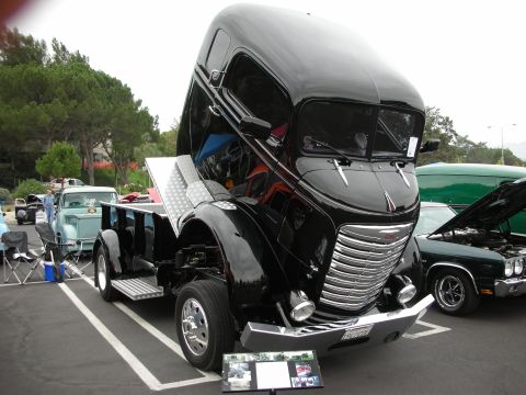 1992 Ford Crown Victoria - A black vintage truck is displayed with its hood open, revealing the engine bay, at an outdoor car show.