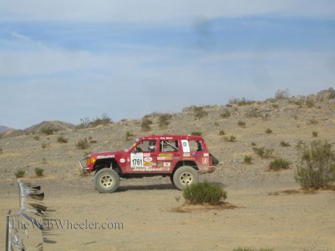 1990 Ford Bronco - red JeepSpeed race SUV marked 1761 races across an open desert landscape with scrub brush and low hills behind it.