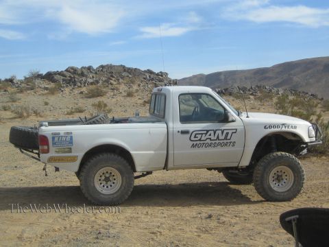 1990 Ford Bronco - white Ford Ranger prerunner pickup lettered Giant Motorsports with a tube rear bumper sits on desert ground near rocks.