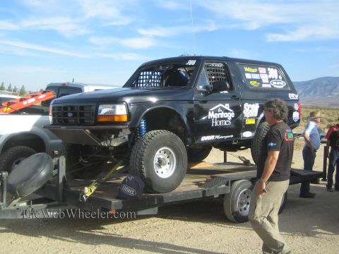 1990 Ford Bronco - black Ford Bronco race truck numbered 300 with Meritage Homes decals sits on a flatbed trailer as a man stands nearby.