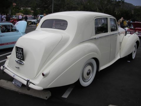 1992 Ford Crown Victoria - A white sedan with a distinctive rounded rear and whitewall tires is parked at an outdoor event.